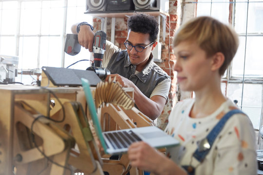 Designers using laptop and power drill in workshop