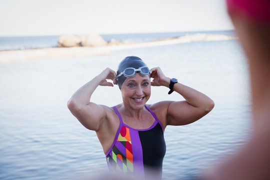 Smiling female open water swimmer adjusting swimming cap goggles in ocean
