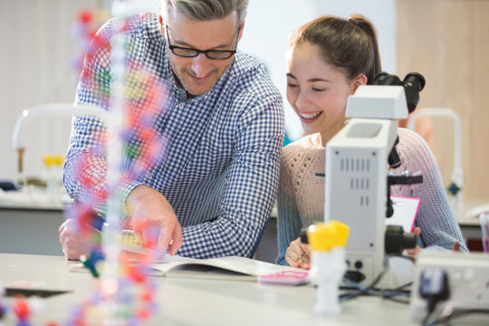 Male teacher helping girl student at microscope in laboratory classroom