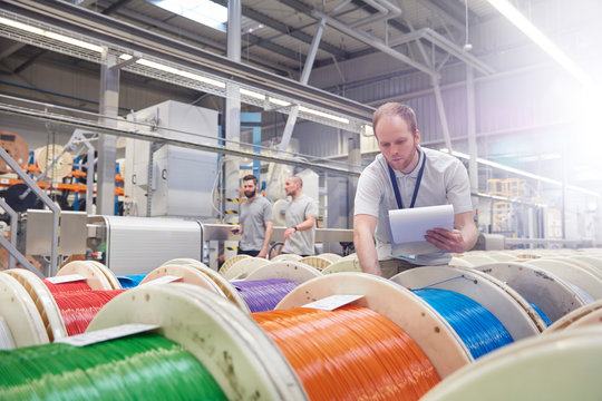 Male worker clipboard checking multicolor spools in fiber optics factory