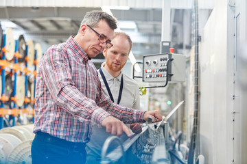 Male supervisor and worker examining machinery in fiber optics factory