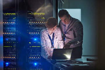 IT technicians working at laptop in dark server room