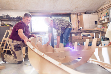 Male carpenters making wood boat in workshop