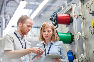 Male female workers digital tablet examining part in fiber optics factory