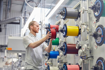 Male worker changing spools on machinery in fiber optics factory