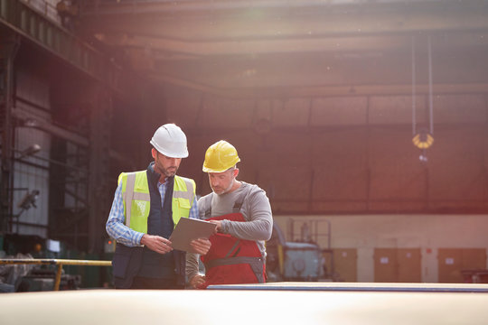 Male foreman and worker with clipboard talking in factory