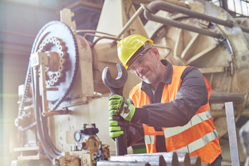 Male worker using large wrench on machinery in factory