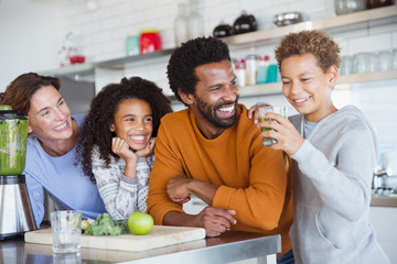 Multi-ethnic family making and drinking healthy green smoothie in kitchen