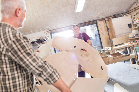 Male carpenters moving wood boat shell in workshop