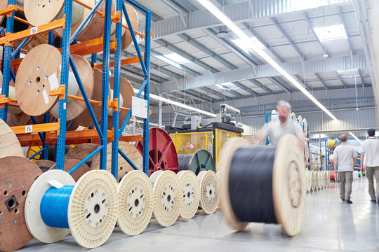 Male worker rolling large spool in fiber optics factory