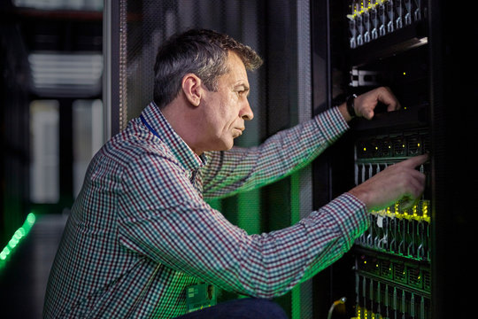 Focused male IT technician working at panel in dark server room