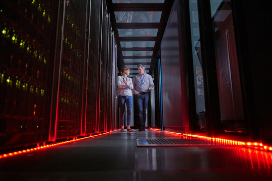 IT technicians talking and walking in dark server room - Powered by Adobe