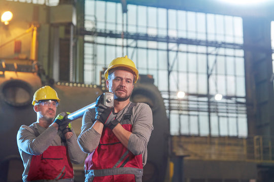 Male workers carrying steel part in factory