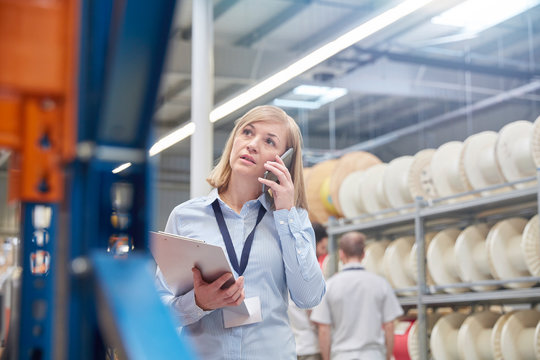 Female supervisor clipboard talking on cell phone in fiber optics factory