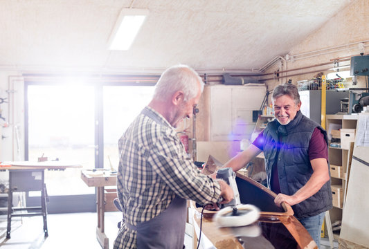 Male carpenters buffing wood kayak with sander in workshop