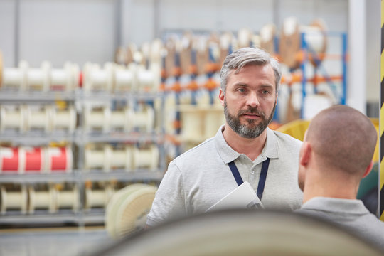 Serious male supervisor listening to worker in fiber optics factory