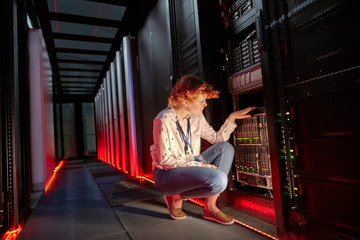 Female IT technician examining panel in dark server room