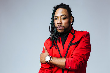 Closeup studio portrait of a man wearing a red jacket suit and dreadlocks
