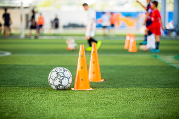 Obraz premium football and marker cones on green artificial turf with blurry soccer team training, blurry kid soccer player jogging between marker cones and control ball with soccer equipment in soccer academy.