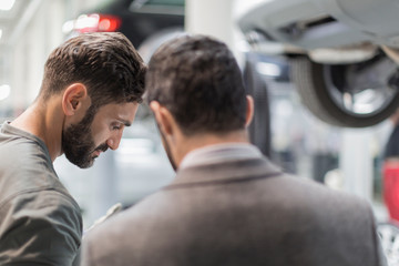 Male mechanic and customer talking, looking down in auto repair shop