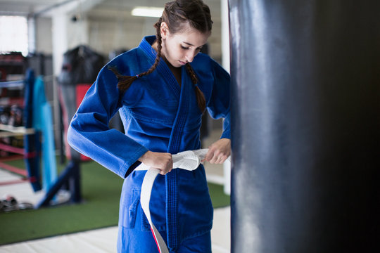 Young woman tightening judo belt at punching bag in gym
