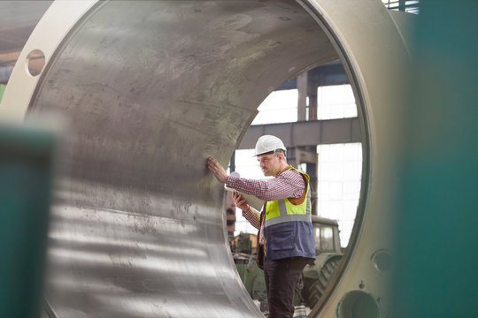 Male engineer examining large steel cylinder in factory