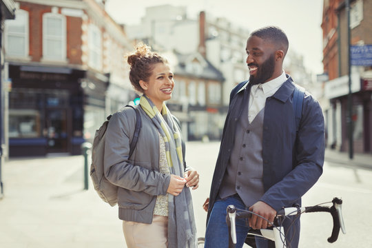 Smiling couple commuting with bicycle on sunny urban street