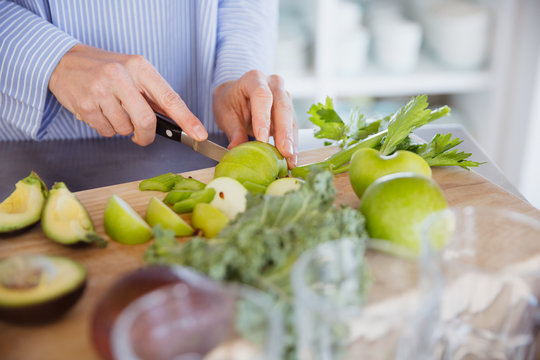 Woman cutting healthy green apples and produce on cutting board