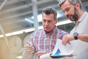 Male supervisors with clipboard examining fiber optic cable in factory