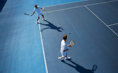 Young male doubles tennis players playing tennis on sunny blue tennis court