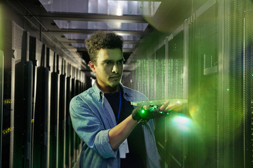 Male IT technician holding glowing futuristic digital tablet in server room