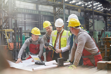 Male foreman, engineers workers with digital tablet meeting in factory