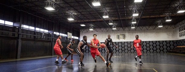 Young male basketball players playing game on court in gymnasium