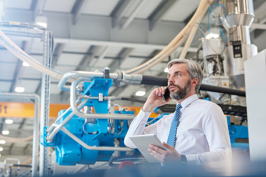 Male supervisor with digital tablet talking on cell phone in factory