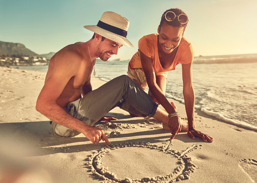 Young couple drawing in sand on sunny summer ocean beach