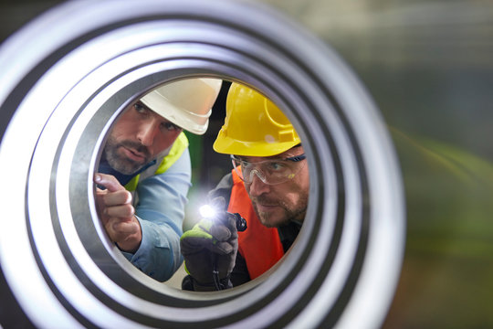 Serious male engineers with flashlights examining steel pipe