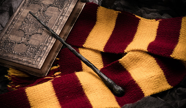Subjects of the school of magic. Scarf, magic wand, book of spells on grey dark rag background.