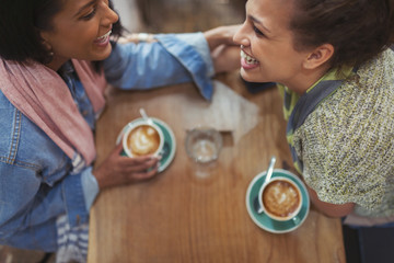 Young affectionate female friends drinking coffee and laughing in cafe