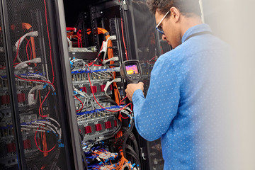 Male IT technician performing diagnostics on panel in server room