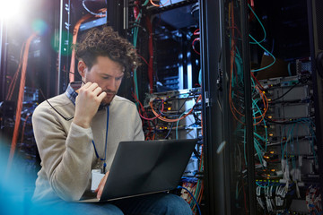 Focused male IT technician using laptop in server room