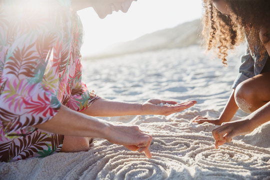 Mother and daughter drawing spirals in the sand on sunny summer beach