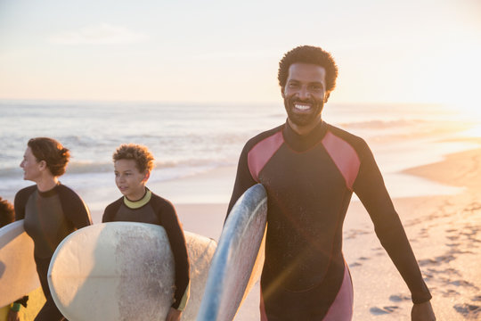 Portrait smiling, confident male surfer carrying surfboard family on sunny summer sunset beach