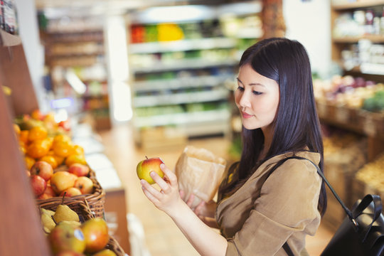 Young woman shopping, examining apple in grocery store