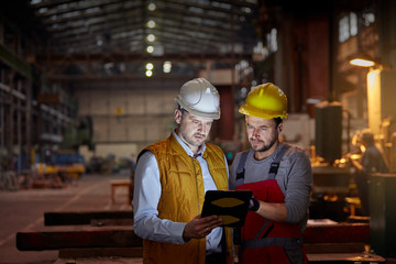 Male foreman and engineer using digital tablet in dark factory