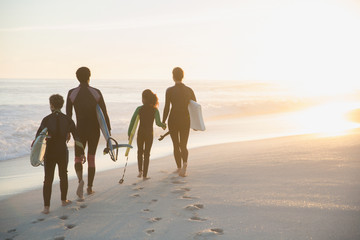 Family in wet suits walking surfboards on sunny summer sunset beach