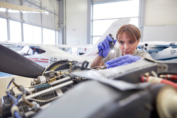 Focused female engineer mechanic flashlight examining airplane engine in hangar