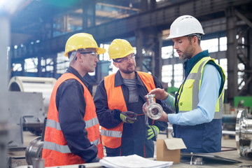 Male engineers discussing steel part in factory