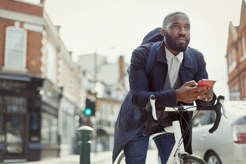 Pensive young businessman texting cell phone, commuting bicycle on urban street