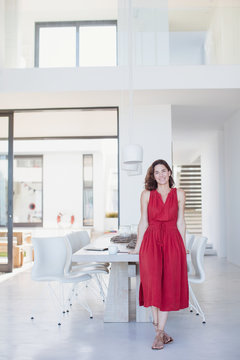 Portrait smiling brunette woman in red dress leaning on dining table