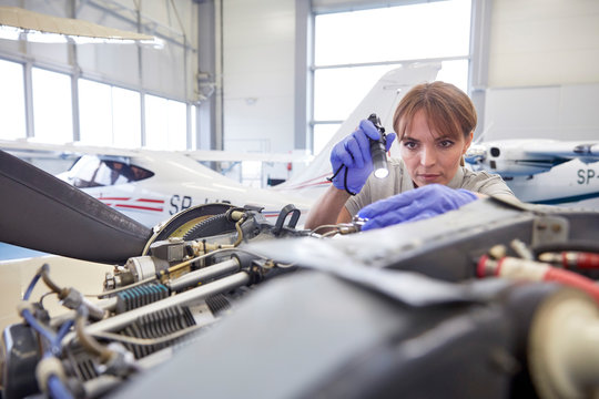 Focused female engineer mechanic flashlight examining airplane engine in hangar